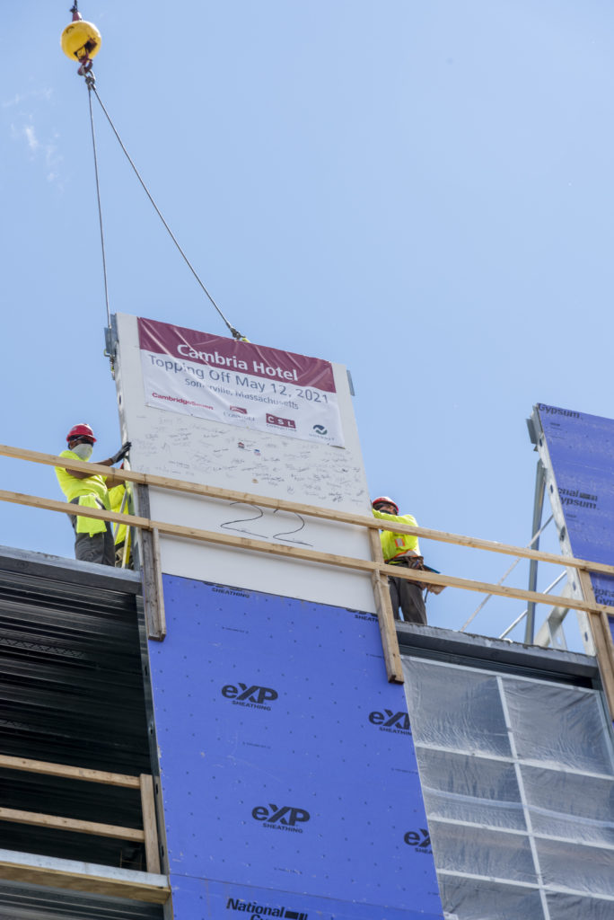 Looking up at a construction crane setting the final piece of steel structure in place on the Cambria Hotel Somerville-Cambridge