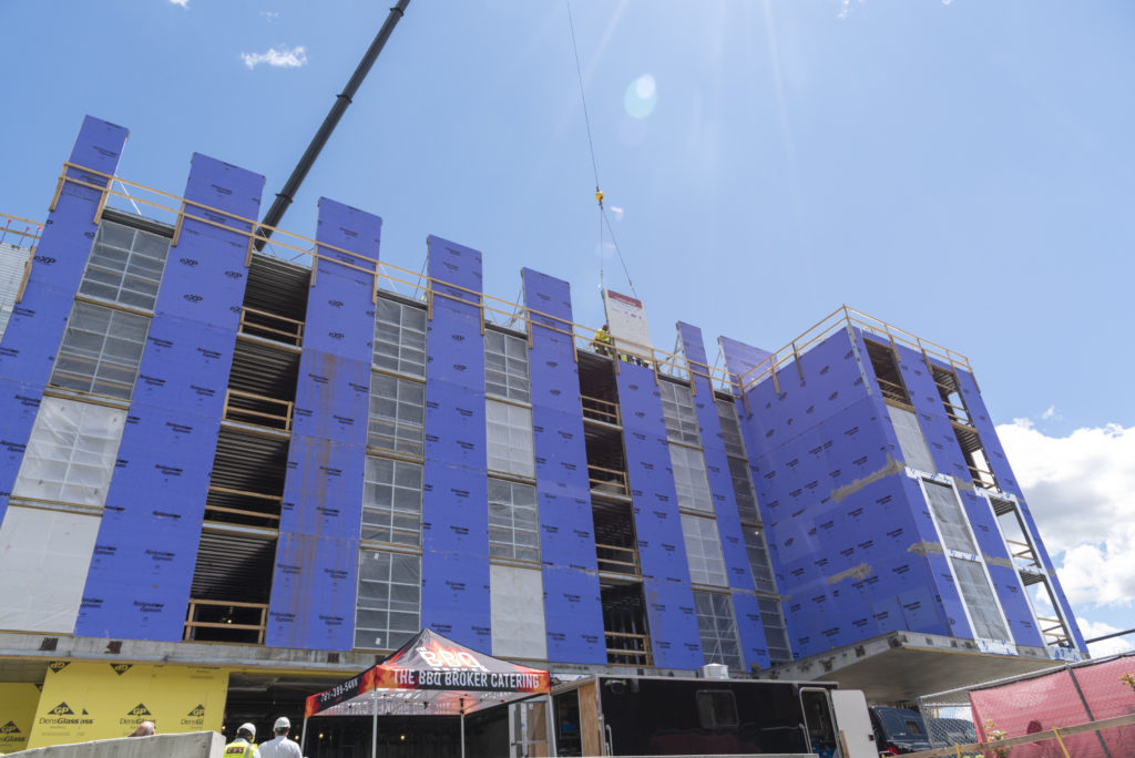 Looking up at a construction crane setting the final piece of steel structure in place on the Cambria Hotel Somerville-Cambridge