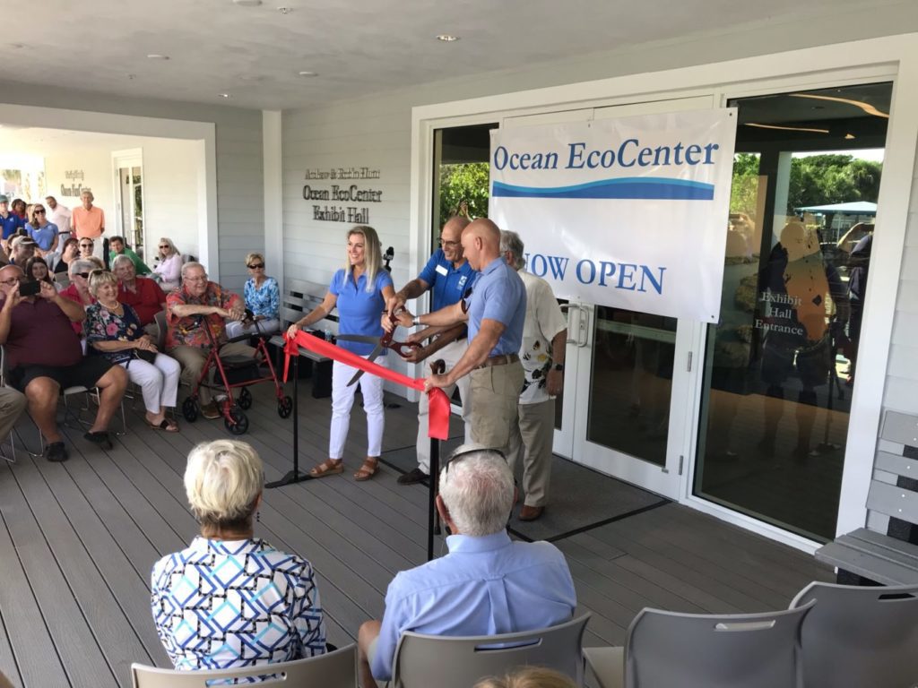 A group of people hold a red ribbon outside on the front deck of the new Ocean EcoCenter in Stuart Florida.