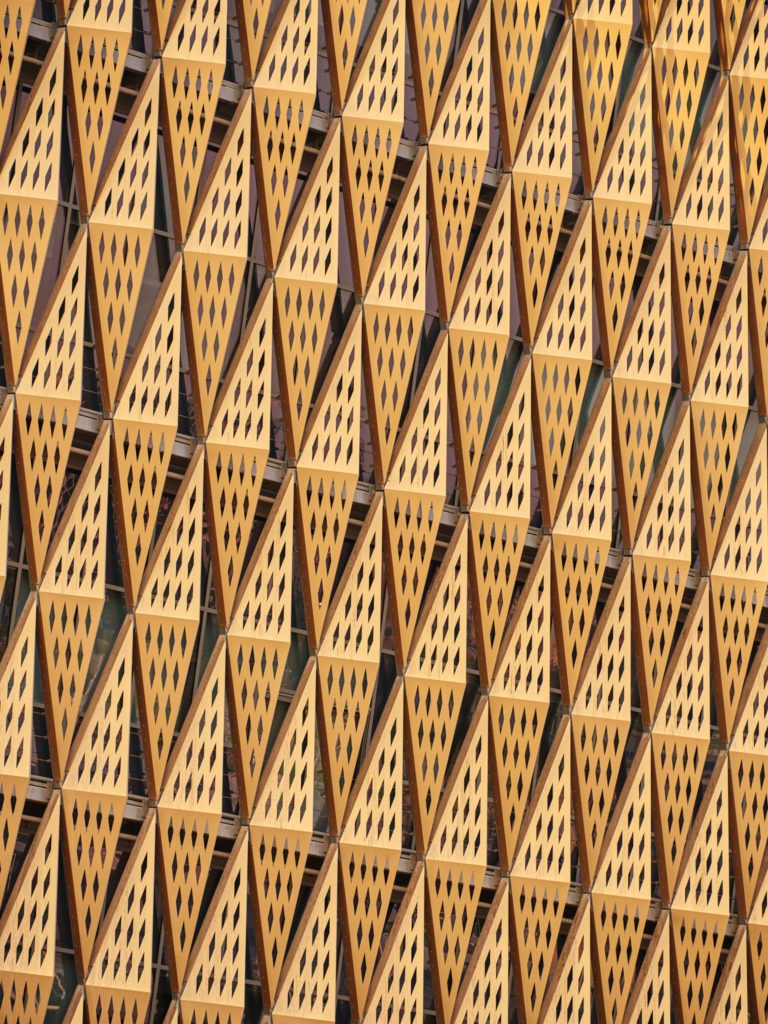 Detail shot of a gold, perforated diamond shaped metal panel facade at Kuwait University